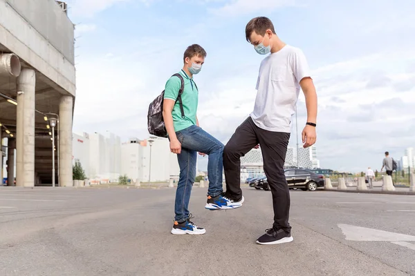 Two friends of teenagers meet in the city. They greet each other with their feet, without contact. The new reality in 2020.