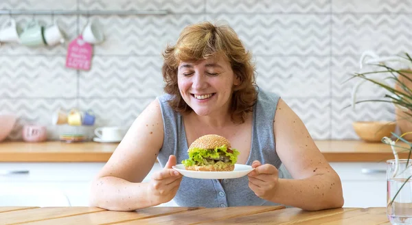 Hamburger tutan mutlu kavisli kadın. Gözleri kapalı ve gülümsüyor. Kız abur cuburu seviyor. Sağlıklı beslenmiyor..
