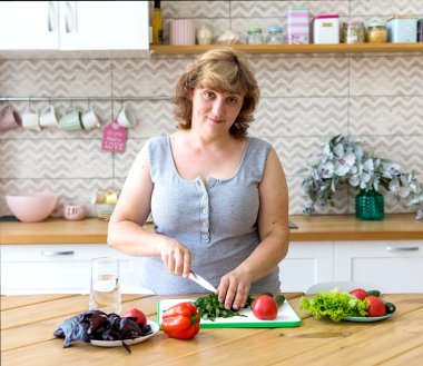 Genç bir kadın mutfağında sebze salatası hazırlıyor. Salatalık, domates ve bitki keser..