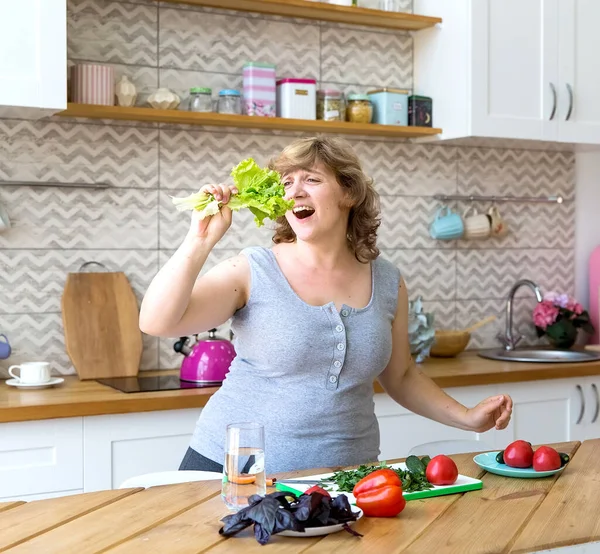 Genç bir kadın mutfağında sebze salatası hazırlıyor. Salatalık, domates ve bitki keser..