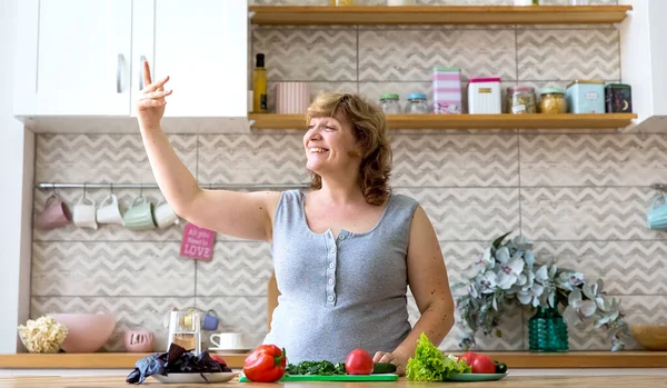 A young woman prepares a vegetable salad in her kitchen. She cuts cucumbers, tomatoes, and herbs.