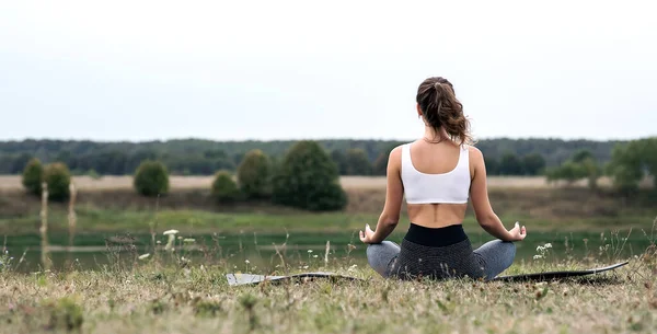 Young sporty woman doing fitness exercises near the river against the background of the forest. Young sporty woman doing fitness exercises near the river against the background of the forest.