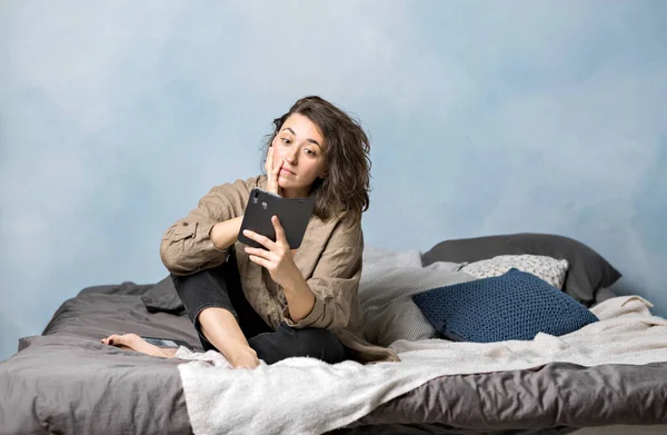 Una Hermosa Morena Está Tumbada Cama Dormitorio Con Smartphone Las — Foto de Stock
