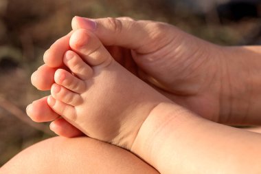 Güneşli bir günde annesiyle yürüyüşe çıkmış bir bebek. Annem onun çıplak bacağını tutuyor. Güzel parmakları var..