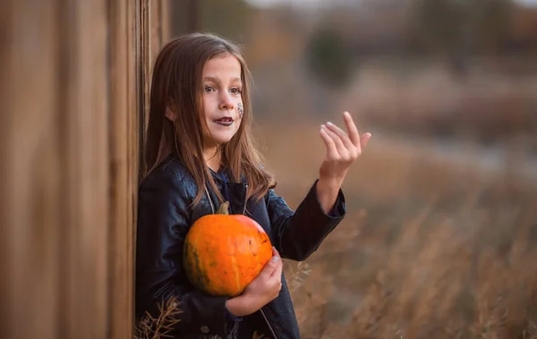 Retrato de una adolescente con ropa oscura sobre un fondo de madera sosteniendo una calabaza naranja. — Foto de Stock