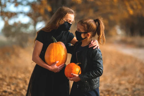 Dos chicas adolescentes con máscaras médicas negras preparan calabazas naranjas para Halloween. — Foto de Stock