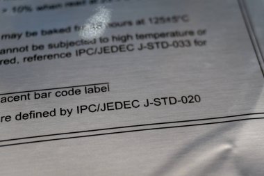 Close-up of moisture barrier vacuum bag caution warning label IPC/JEDEC J-STD-020 standard reference from electronics manufacturing industry clipart