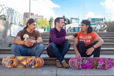 Mor gömlekli beyaz adam. El mikrofonuyla röportaj. Uzun saçlı, İspanyol kaykaycı, turuncu tişörtlü.