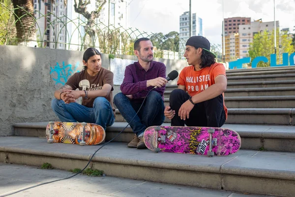 Kaukasischer Mann Lila Hemd Interviews Mit Handmikrofon Junger Langhaarspanischer Skateboarder — Stockfoto