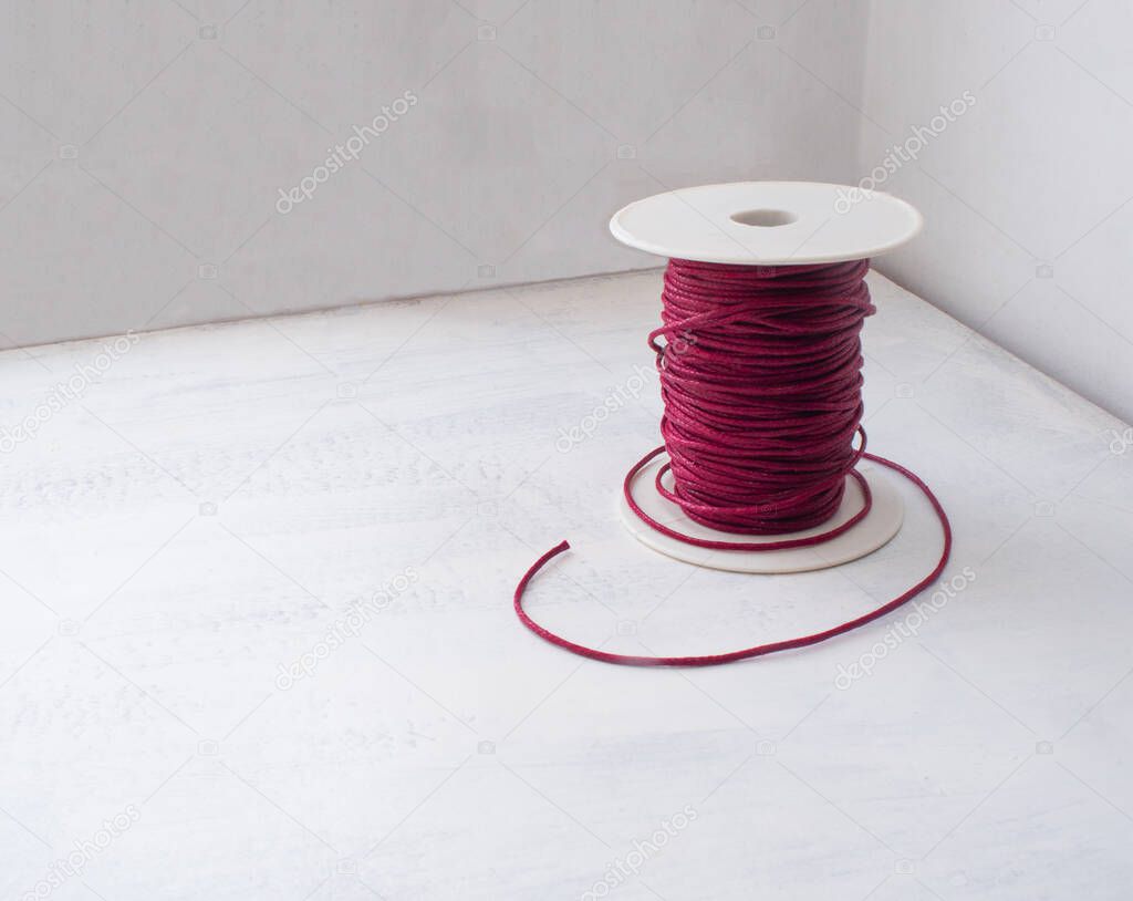 Dark Red Waxed Thread and a Rustic Jute Skein Thread on a White Table and White Wall Background
