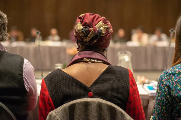 Woman with a Headscarf in Front of a Table full of People