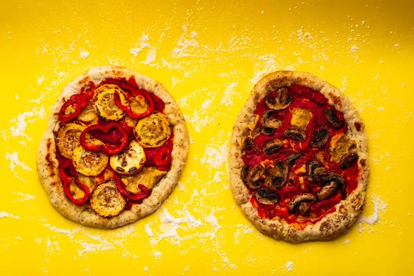 Rustic and Homemade Vegan Pizzas, One with Mushrooms and other Zucchini and Bell Peppers on a Yellow Background