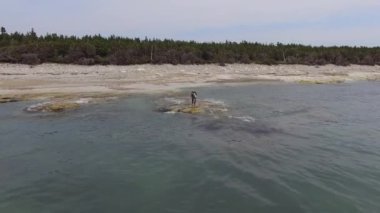 Anticosti Adası, Quebec / Kanada - 8 Temmuz 2018: Sahilde, Ormanın Yakınındaki Genç Adam, Suya Girer, Atlantik Okyanusundaki fokların fotoğraflarını çekmek için Kayalıklarda Yürür
