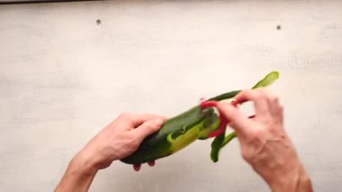 Beyaz adamın eli, arka planda sebze soyacağı olan bir salatalığı soyuyor.