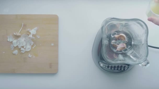 メデリン アンティオキア コロンビア 2020年1月9日 ホワイトマンの手がホワイトテーブルのカッティングボードの横にあるブレンダーにいくつかのニンニクの上にレモンジュースを投げます — ストック動画