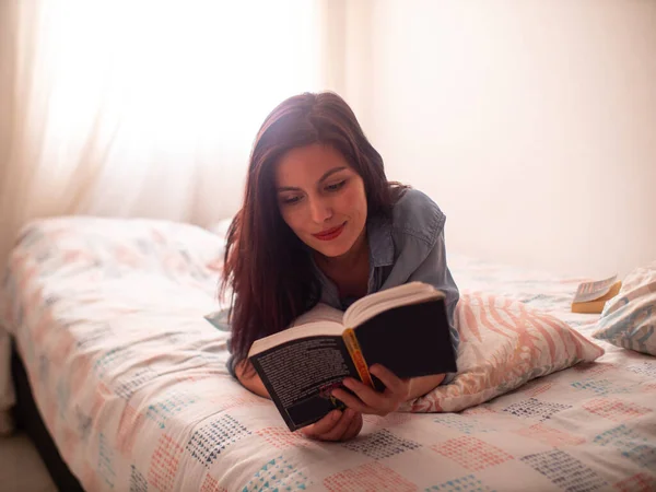 Молодая Латиноамериканка Читает Книгу Лежащую Кровати Поддерживаемую Подушкой Листьев — стоковое фото