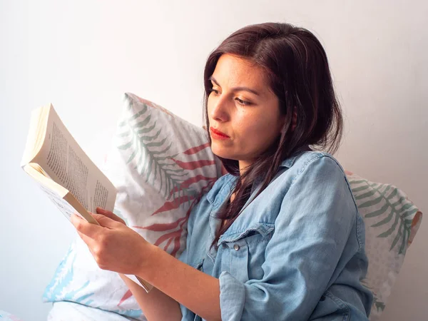 Молодая Испаноязычная Женщина Читает Большую Книгу Сидя Белой Стене Листовой — стоковое фото