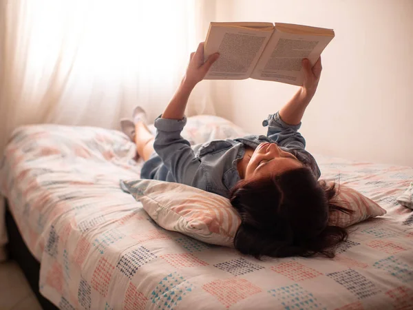 Молодая Латиноамериканка Читает Книгу Лежащую Кровати Поддерживаемую Подушкой Листьев — стоковое фото