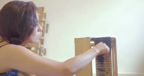 黒い服を着た若いヒスパニック系の女性がパレットの背景を持つ黒の木の箱を描く — ストック動画