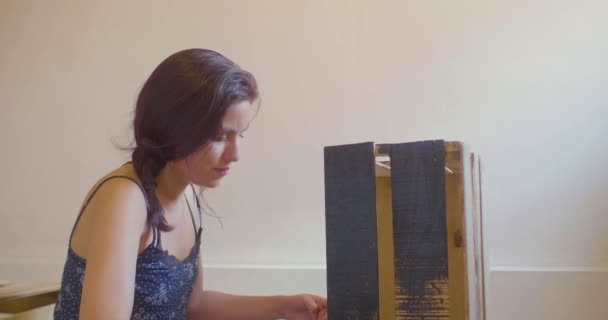 黒い服を着た若いヒスパニック系の女性がパレットの背景を持つ黒の木の箱を描く — ストック動画