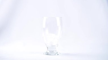 Beyaz zemin üzerinde buz küpleri olan cam bardağa biraz alkol ya da su dökülür.