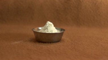 Bir kadının eli kahverengi bir zemine küçük bir tabak pudra sütü koyar.