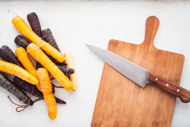 Kesme tahtasındaki bıçağın yanında mor ve sarı havuçlar.