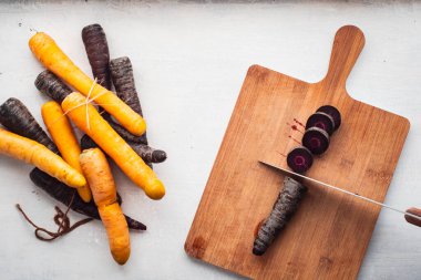 Mor ve Sarı Havuçlar Bıçaklı Kesme Tahtasının yanında Havuçları Beyaz Arkaplanda Parça Parça Parça Kesiyor