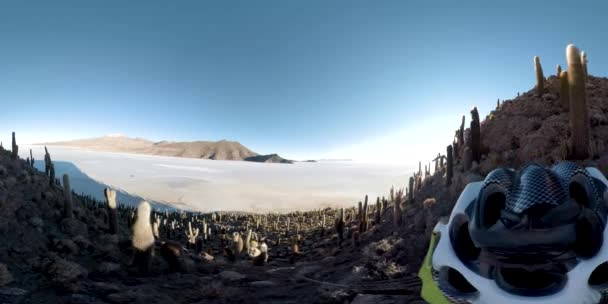 ヘルメット中の人の360度の眺め世界最大の塩平であるウユニ塩湖のサボテンでいっぱいの山を下ります — ストック動画