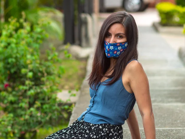 西班牙裔年轻女子头戴蓝色花脸面具坐在人行道上 — 图库照片