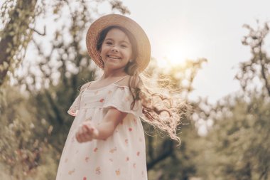 Gün batımında parkta gülümseyen ve mutlu genç kız portresi. Neşeli modern çocuk modeli yazın bahçede poz veriyor.