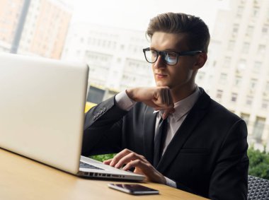 Her zaman müsait. Güzel genç iş adamı dizüstü bilgisayarıyla çalışıyor ve dışarıda masada otururken telefonla konuşuyor.