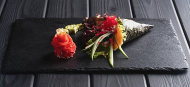 Suşi, nigiri ve suşi siyah arka planda soya sosu ve çubuklarla koyu taş tabakta yuvarlanır..