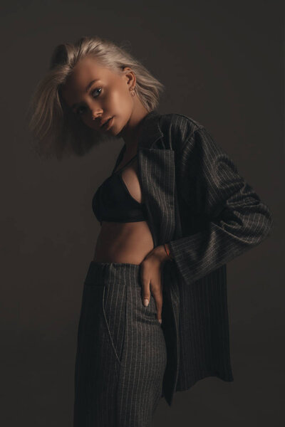 Соблазнительный портрет молодой сексуальной девушки с светлыми волосами в нижнем белье и классический костюм на черном фоне в номере
