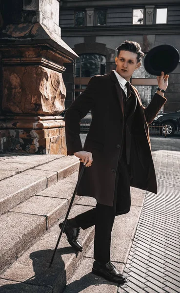 Stijlvolle jongeman in klassieke jas en pak met stok op stedelijke achtergrond. Trendy knappe jongen model lopen op straat — Stockfoto