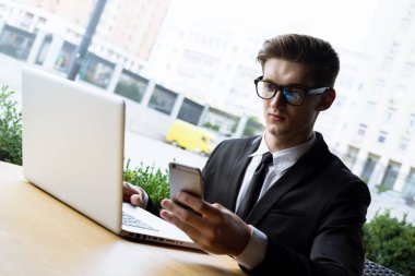 Her zaman müsait. Güzel genç iş adamı dizüstü bilgisayarıyla çalışıyor ve dışarıda masada otururken telefonla konuşuyor.