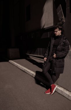 Siyah ceket ve pantolon, kırmızı spor ayakkabı, sırt çantası, gözlük giyen moda güzel adam. Sokak şehir tarzı 
