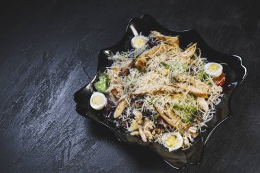 Lezzetli taze sezar salatası, siyah bir tabakta siyah bir masa arkasında tavuk ve yumurta.