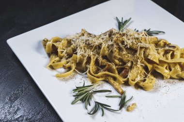 Beyaz bir tabakta siyah bir masa üzerinde nefis bir makarna.