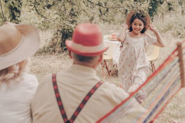 Bahçede yaşlı çift hamakta arka manzarada oturuyorlar. Kırmızı şapkalı büyükbaba büyükannemi sever. Mutlu yaşlılık. Genç torun onlara koşar.