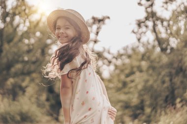 Mutluluk anı. Günbatımında parkta modern, güzel, mutlu bir çocuk. Üzerinde elbise ve şapka vardı. Yazın bahçede güzel gülümseyen genç kız modeli.