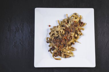 Lezzetli taze carbonara makarnası. Beyaz tabakta servis ediliyor. Arka planda siyah bir masa var. 