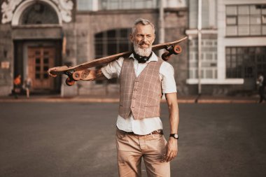 Kaykaylı şık hippi sakallı adam. Günlük kıyafetlerle yetişkin modeli şehir caddesinde uzun tahta sürüyor. Sokak yaşamı spor fotoğrafı.