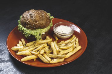 Sarımsak soslu taze patates, siyah bir masada kırmızı tabakta sulu bir sebze burger. 