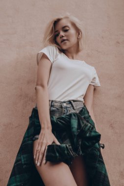 Turuncu duvarın yanında poz veren şık bir kız. Güzel baştan çıkarıcı seksi kadın günlük giysiler içinde şehir sokaklarında yürüyor.