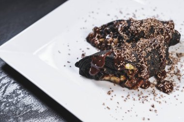 Çikolatalı ve muzlu leziz taze gözlemeler, siyah taş bir masada beyaz bir tabakta tarçın.