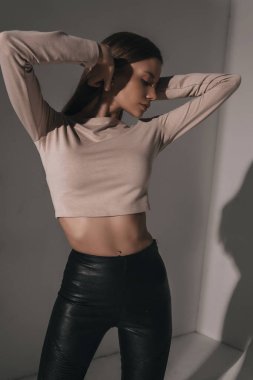 Beyaz arka planda odada poz veren güzel, baştan çıkarıcı bir kadın. Deri pantolon ve reglan giyen çekici seksi manken. Güzel bir portre.