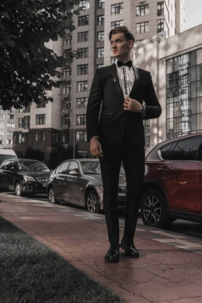 Handsome stylish businessman posing on street. Young man model walking on building background. Success lifestyle. Business concept