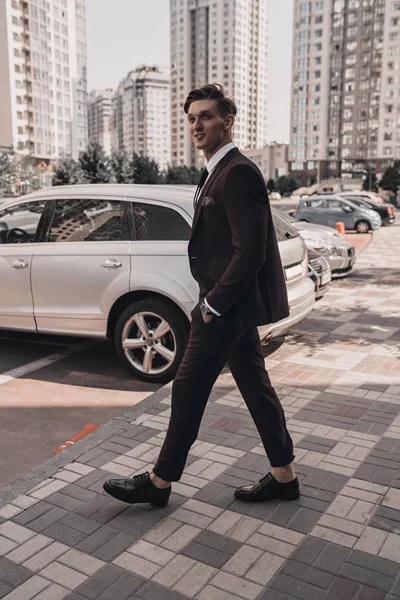 Stylish handsome male model posing on city street. Young success businessman in full suit on urban background. Cityscape. Business concept