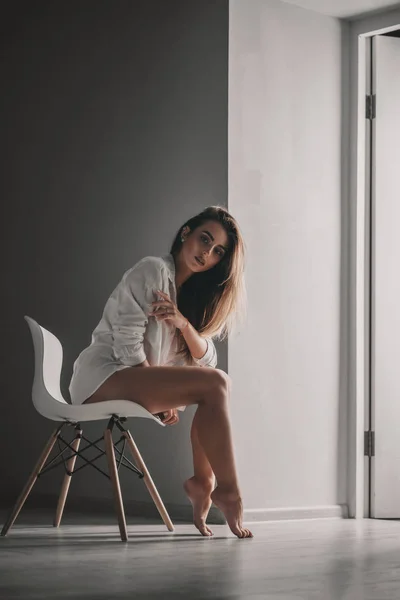 白いシャツを着た美しい体と部屋の椅子にポーズをとる下着のきれいな女の子 セクシーな現代女性モデルスタイリッシュな肖像画 — ストック写真